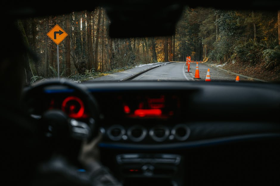 View from car dashboard of rural road with traffic cones and turn sign. Scenic forest driving experience.